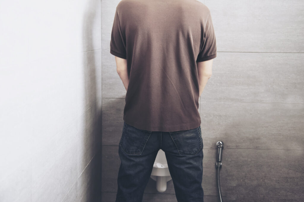Hombre orinando en un baño, asociado a aumento de la frecuencia urinaria