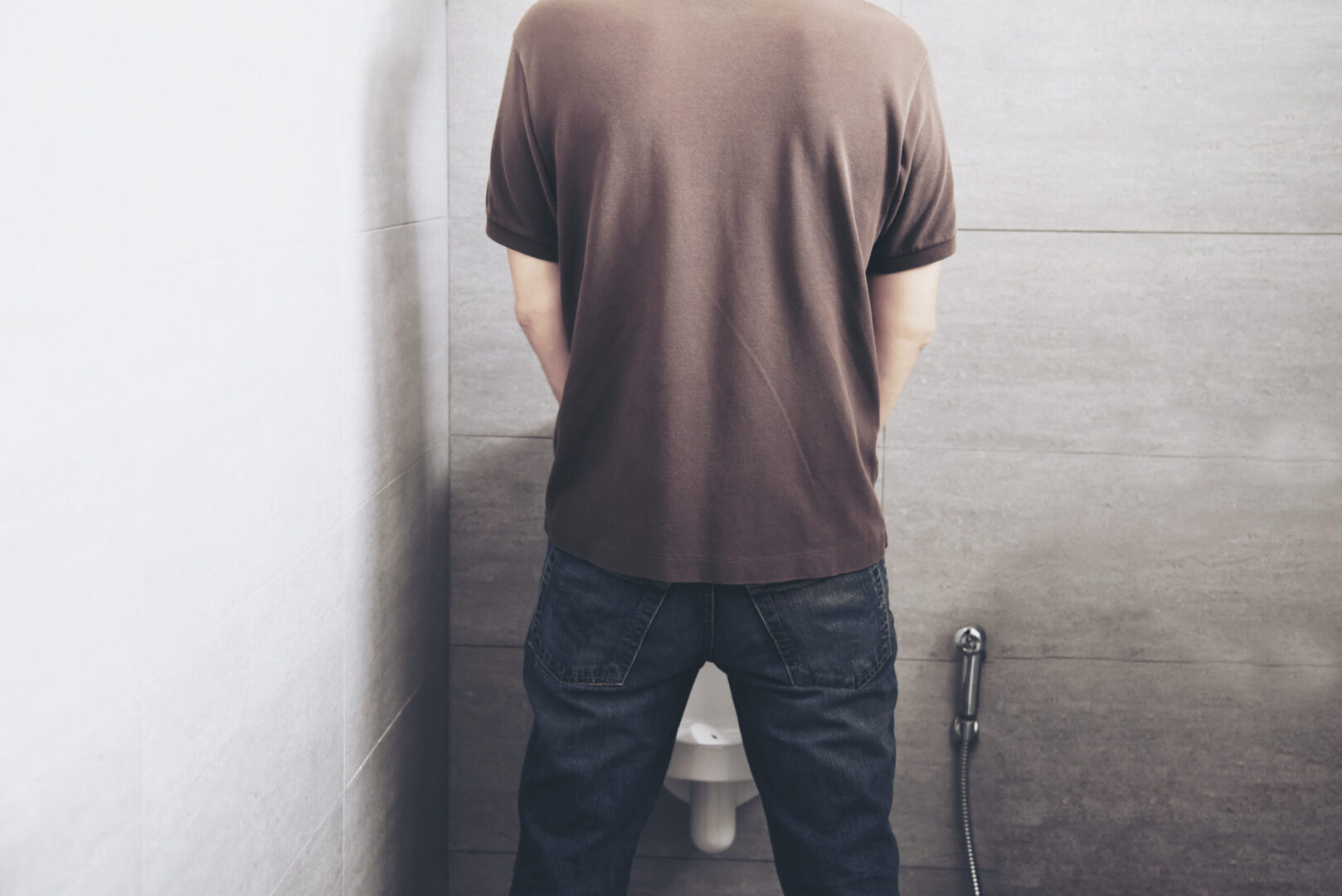Hombre orinando en un baño, asociado a aumento de la frecuencia urinaria